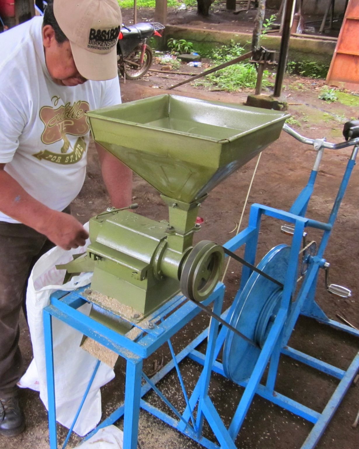 The fully assembled machine, painted blue with a green dehuller mounted. A belt connects the flywheel to the dehuller.