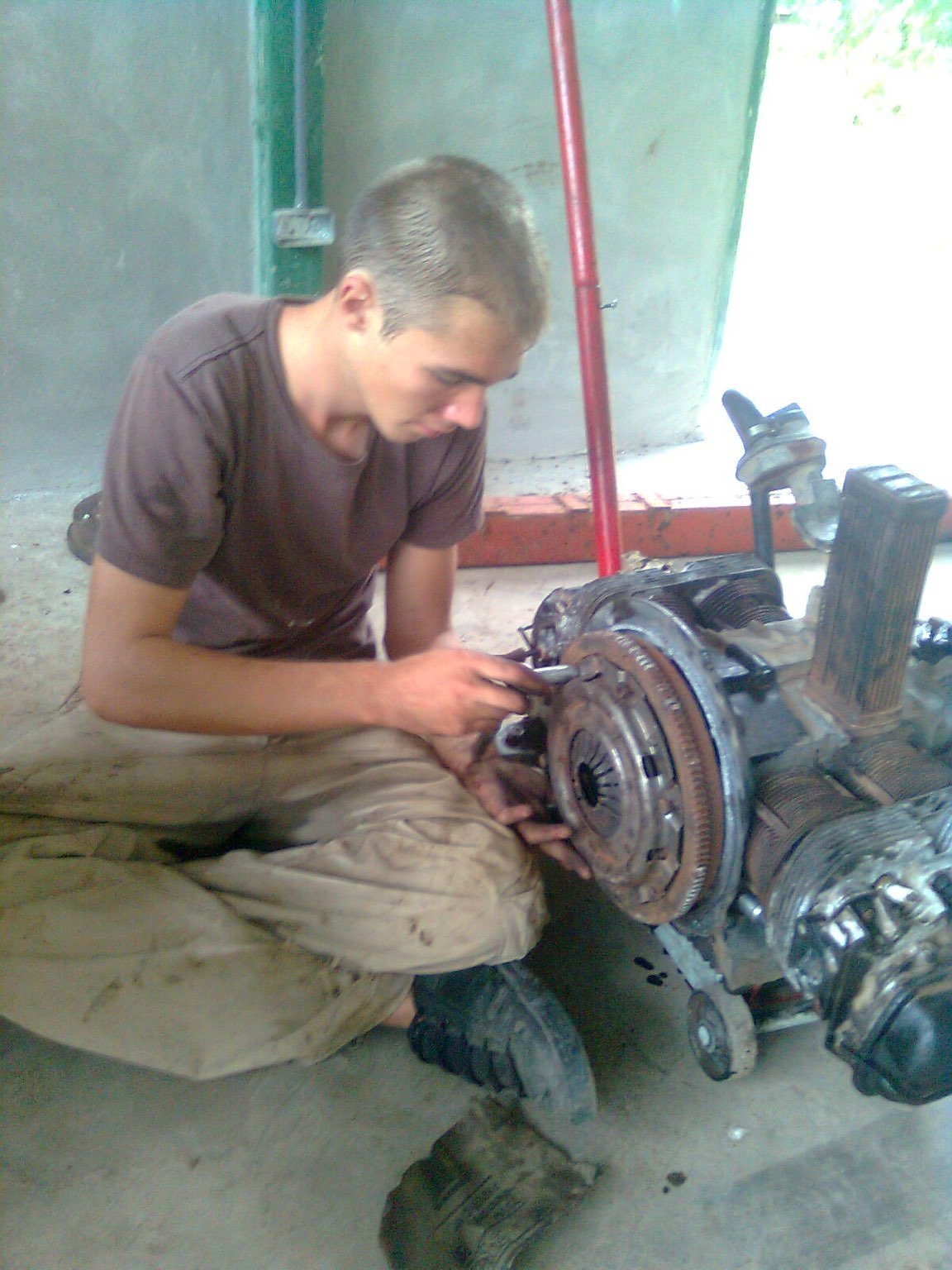 Mechanic shop with car parts everywhere. A person inspects the engine supported by a jack.